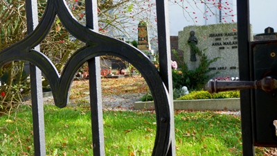 Blick durch das gusseiserne Gitter auf die Gr&auml;ber am Friedhof Kaufering Dorf